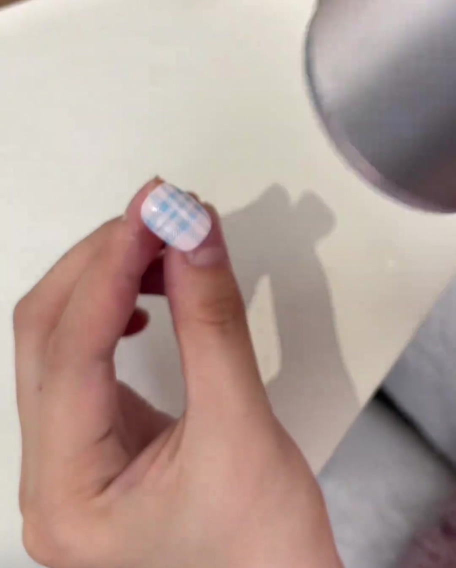 Clear crystal powder being sprinkled over a stamped blue plaid pattern on a nail using a metal cuticle pusher.