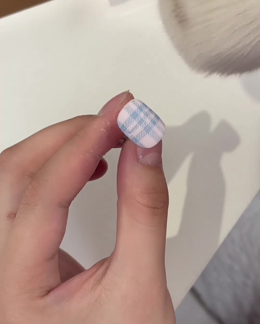 A fluffy makeup brush sweeping excess white crystal powder off a cured plaid-patterned nail.