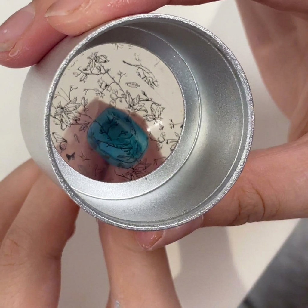 A clear jelly stamper held over a turquoise nail, showing the black floral pattern positioned for transfer.