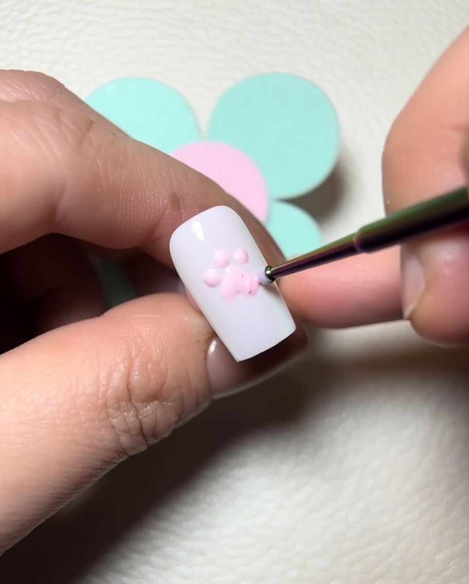 A detail brush applying clear sculpting gel over the pink toe beans to add dimension.