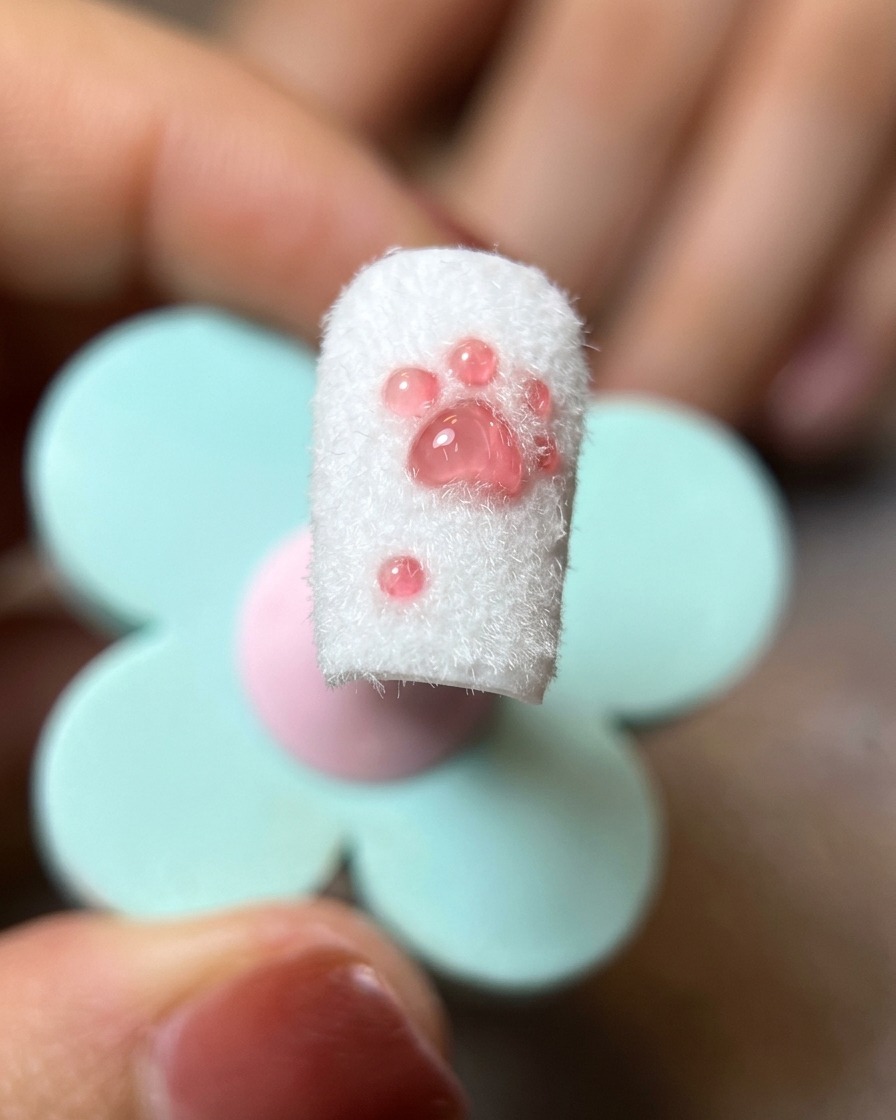 A close-up of a finished cat paw nail design with the excess flocking powder being brushed off by a soft-bristled brush.