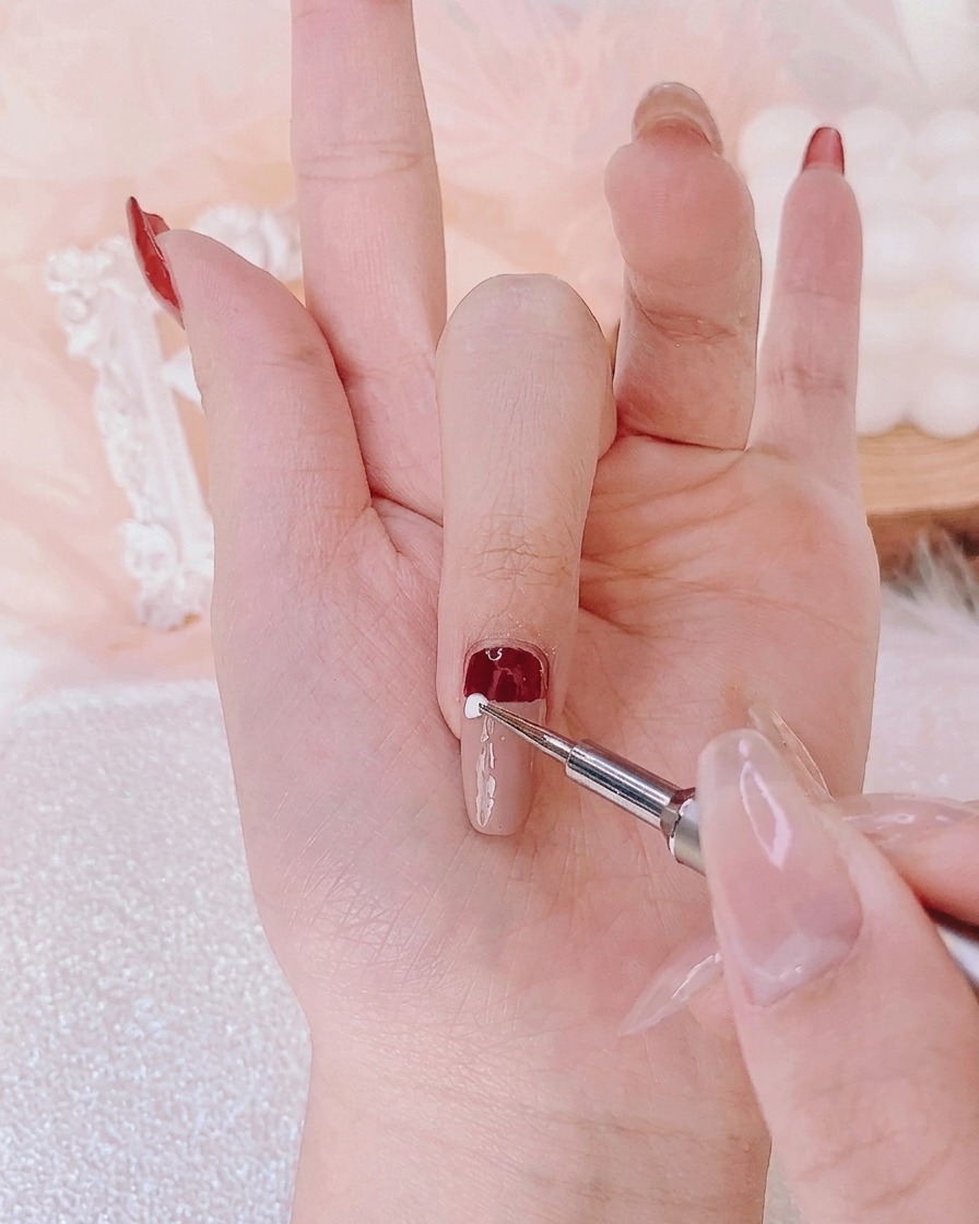 A dotting tool applying a precise dot of white gel onto the center of a nail to form a design element.