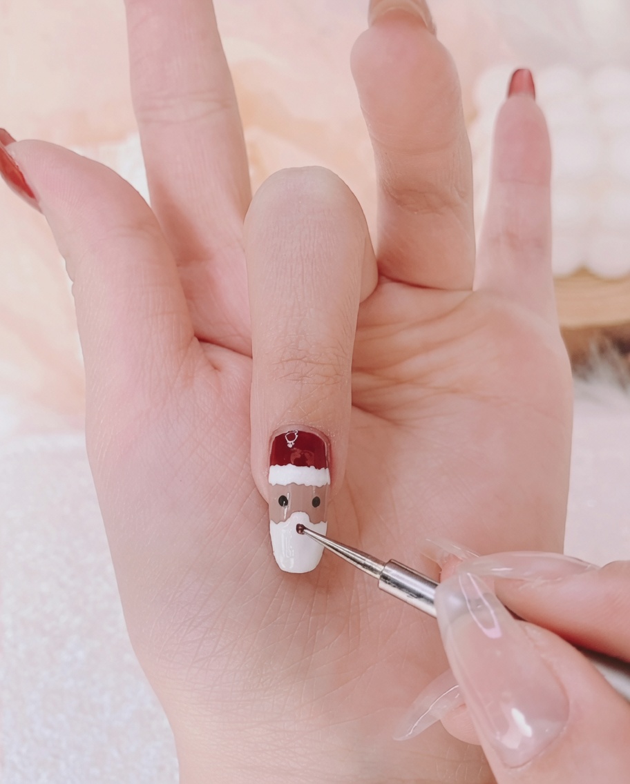 A fine liner brush adding two tiny black dots to a nail to represent character eyes.