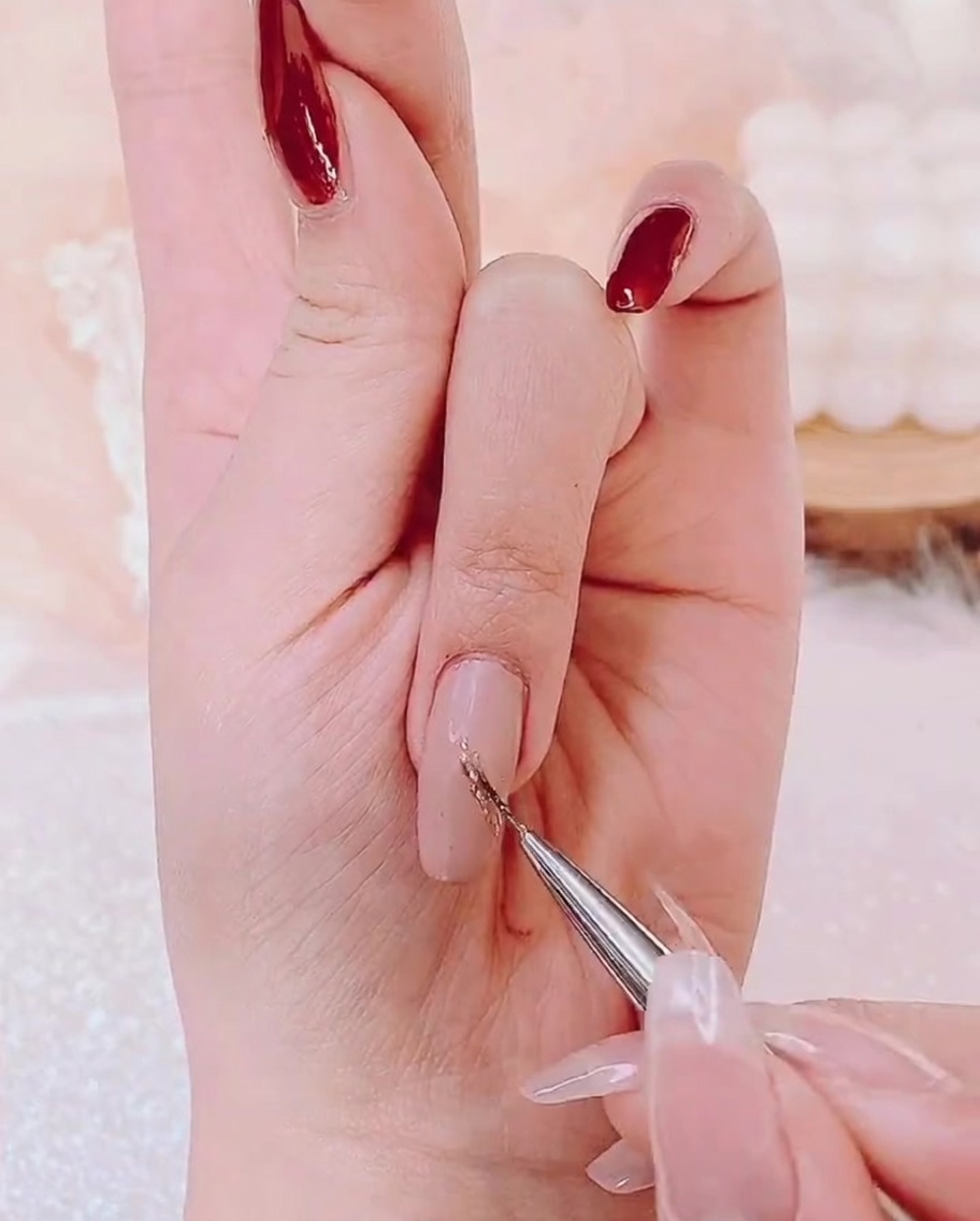 A detail brush applying a thin layer of gold shimmer gel to the center of a nail.