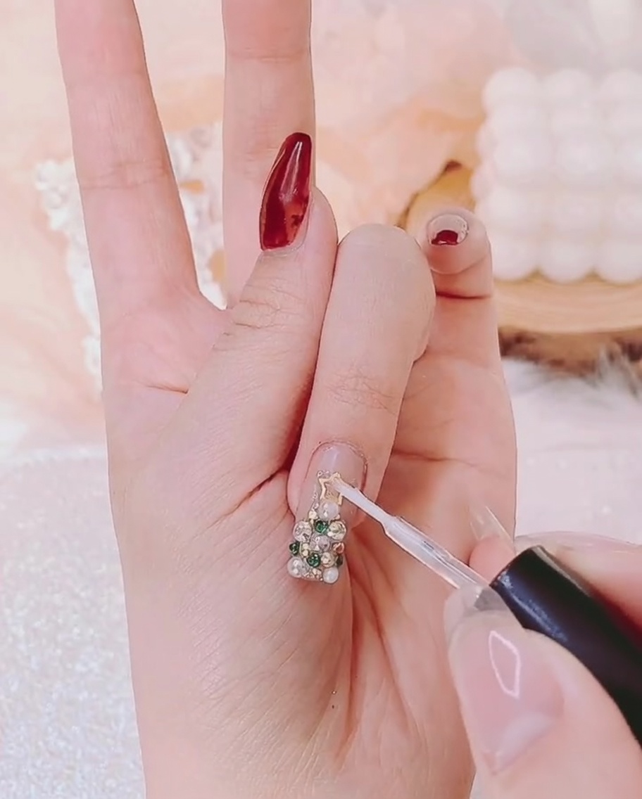A fine detail brush applying clear top coat gel around the edges of 3D nail art embellishments.