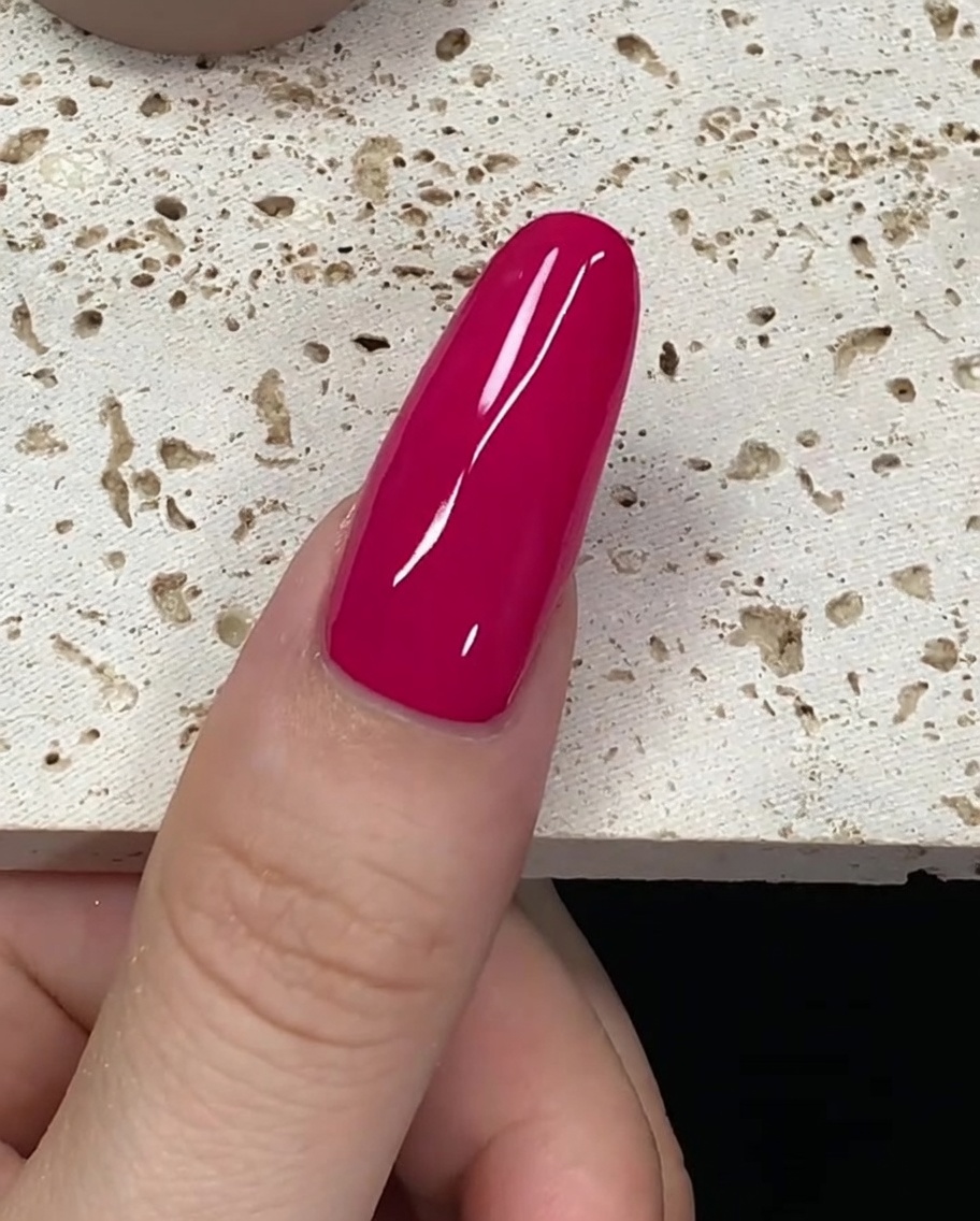 A brush loaded with deep red gel polish hovering near the cuticle of a nail.