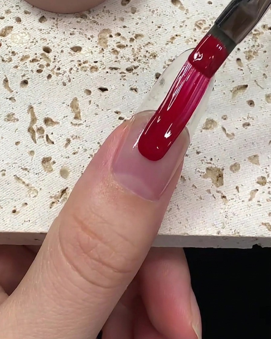 A smooth application of deep red gel polish being pulled down the nail plate.