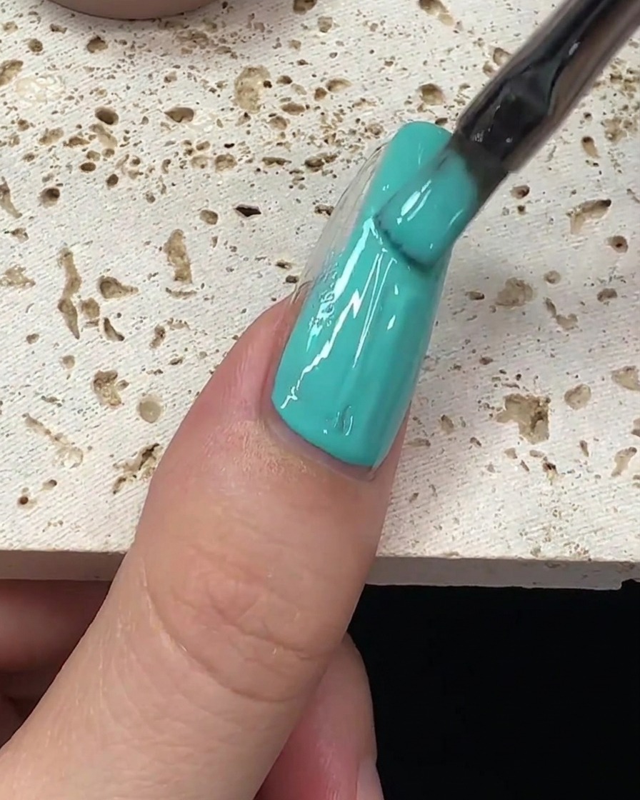 A brush stroke of mint green gel polish being pulled down the center of the nail.