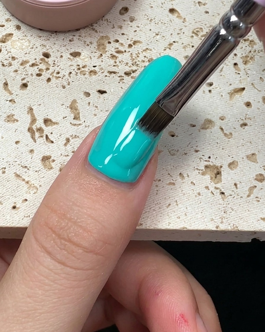 A close-up showing the final strokes of mint green gel polish smoothing out to the end of the nail.