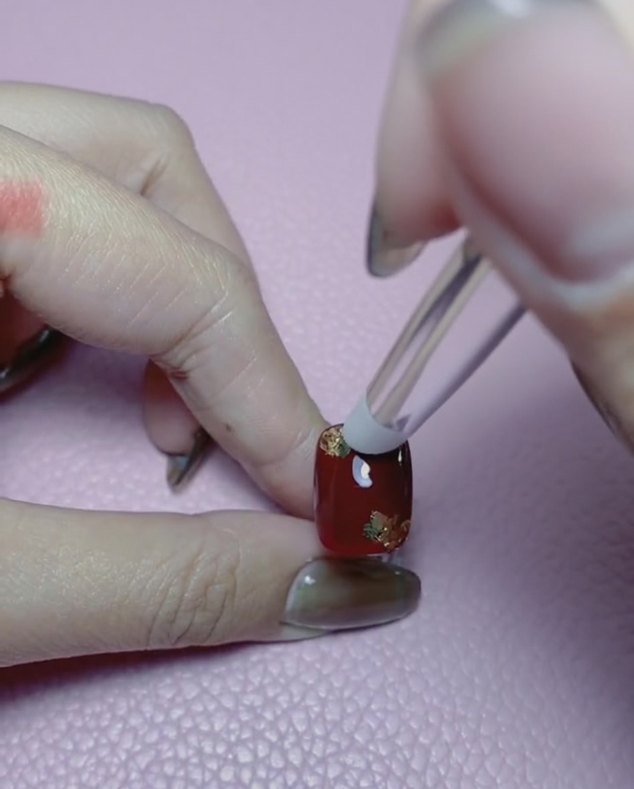 Close-up of a silicone tool smoothing out gold foil over a red nail.