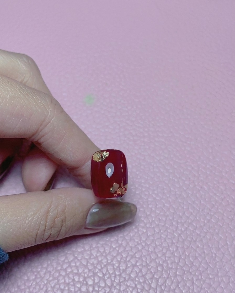 Close-up of a red nail with gold foil accents, covered in a high-gloss top coat.
