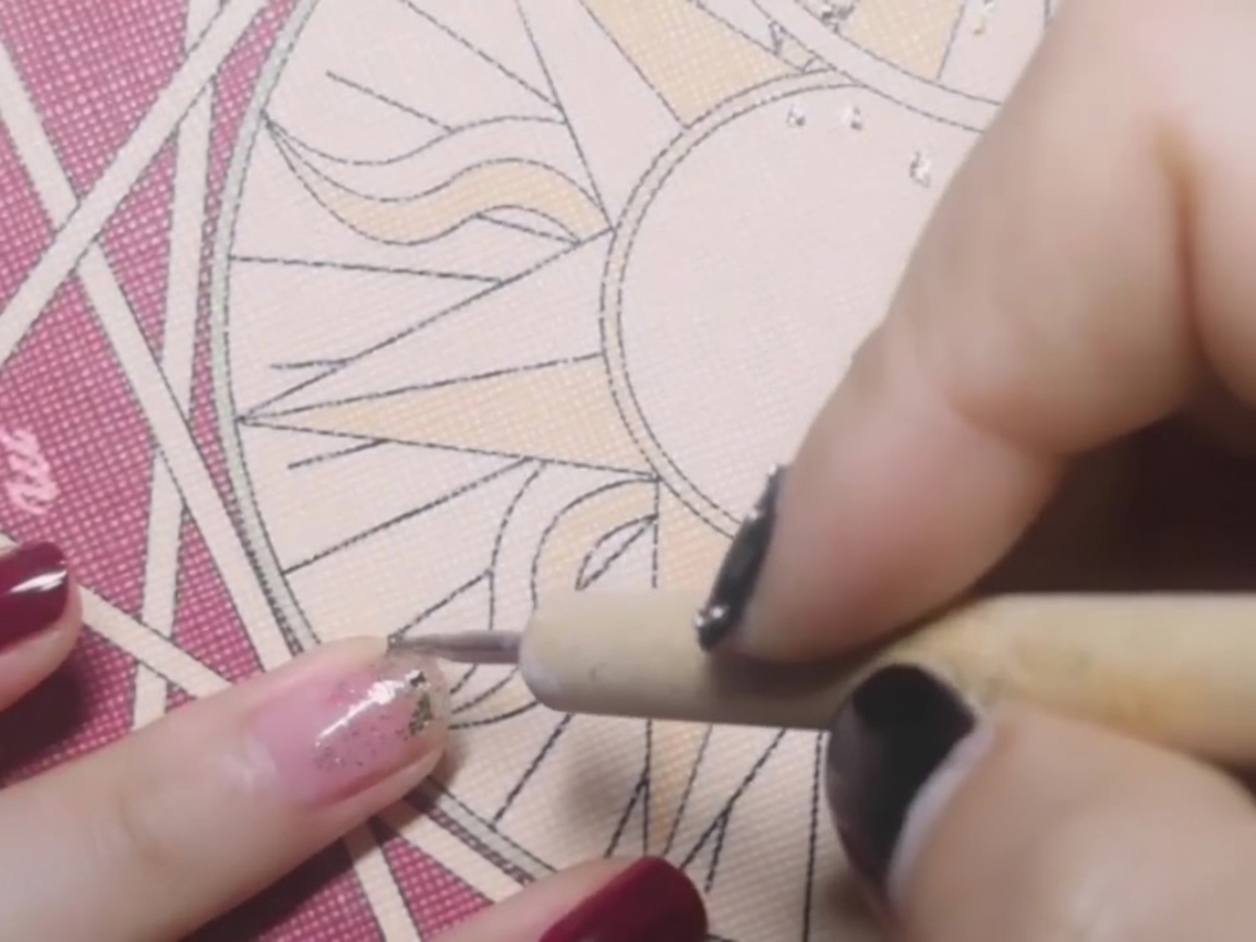 A dotting pen placing a delicate flake of gold foil onto the center of a nail coated in tacky base coat.