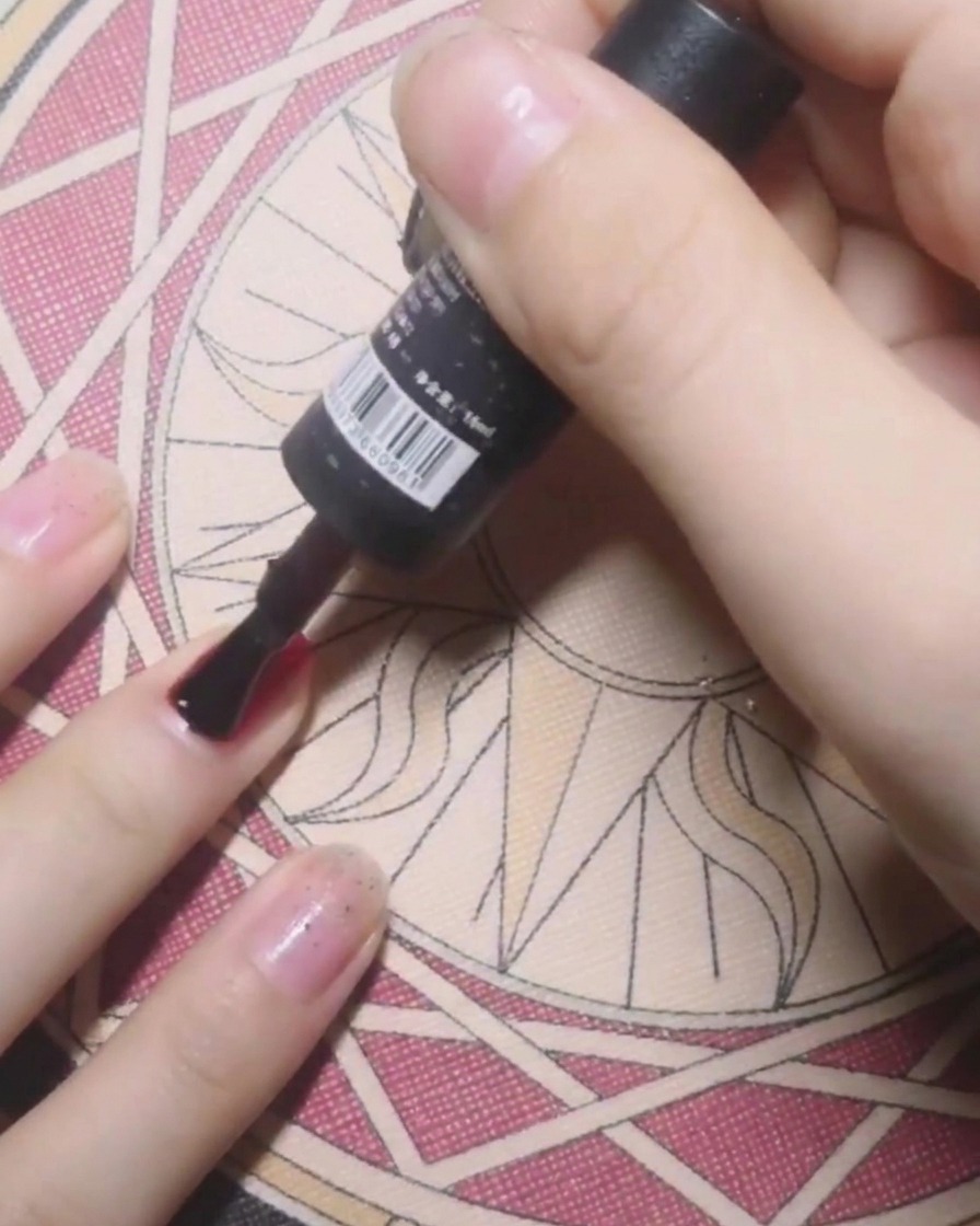 A bottle brush applying clear base coat to a nail in preparation for solid red gel polish.