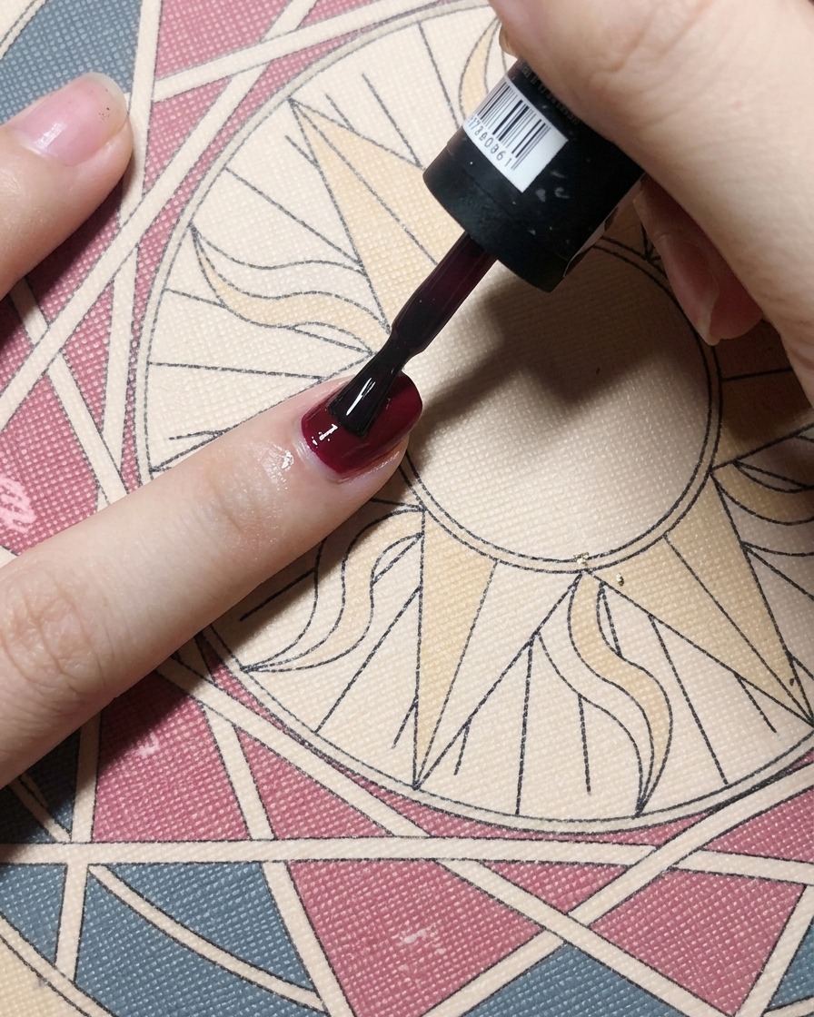 A brush applying a rich, deep red gel polish over a nail base coat, creating a solid opaque color.