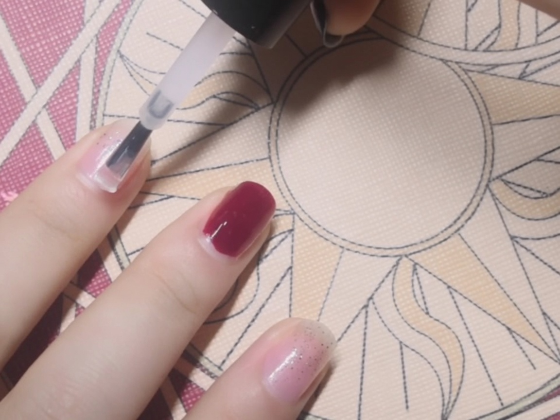 A close-up of a clear base coat being applied with a brush to a fingernail.