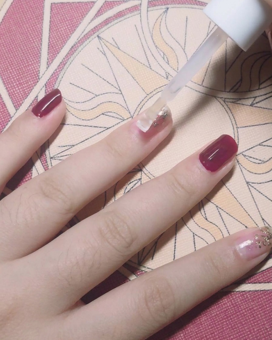 A brush applying a clear top coat over a nail decorated with gold foil flakes.