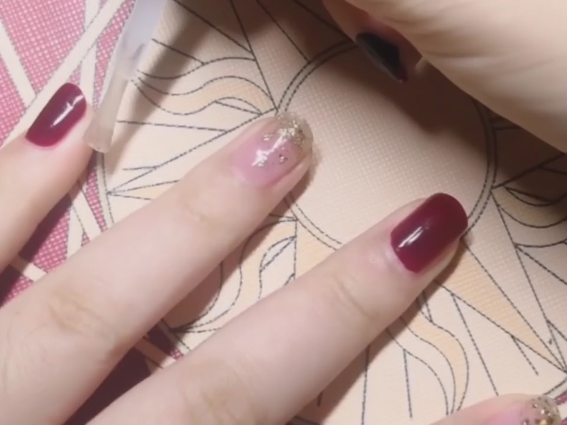 A clear top coat being applied over a solid red nail.