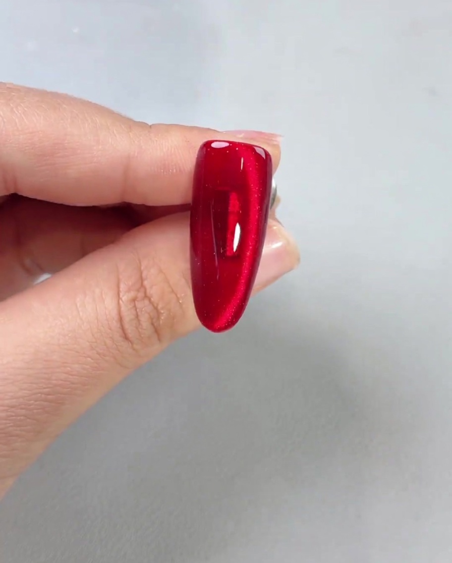 A glossy top coat being applied to a finished red magnetic nail, showing high shine.