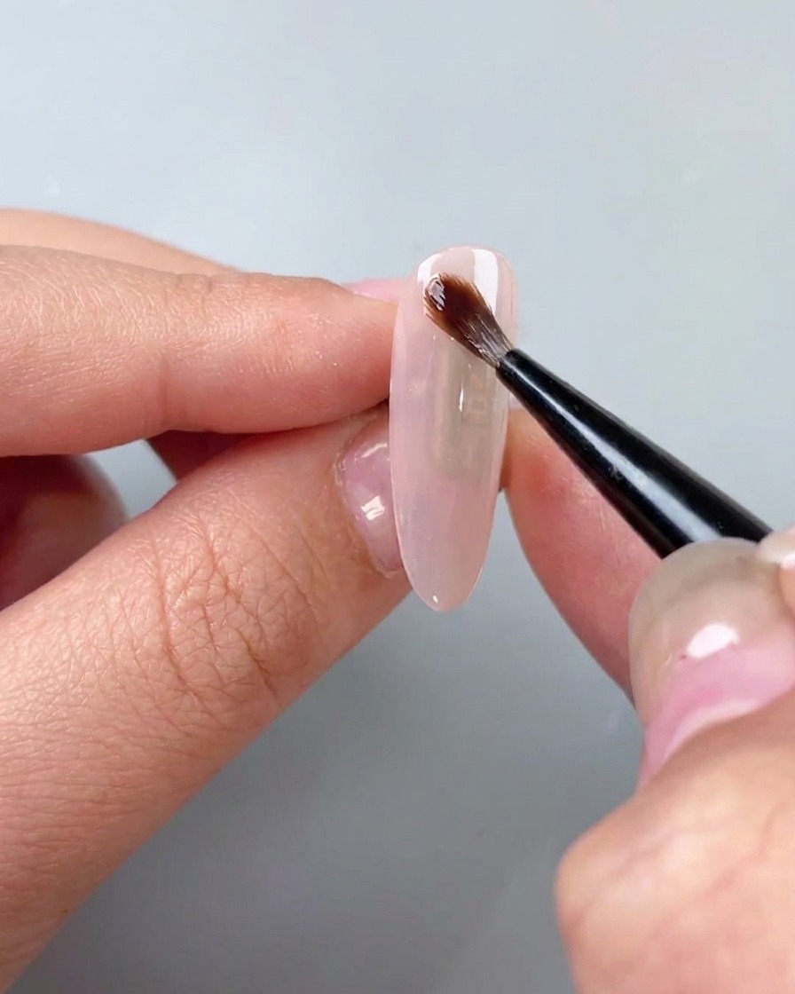 A brush applying a clear watercolor blooming gel over a base coat.