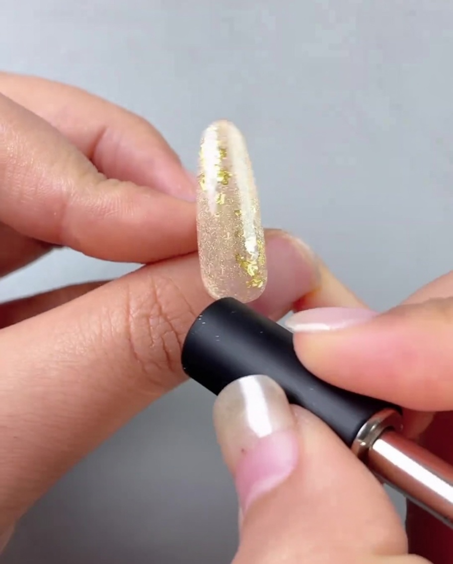 A nail magnet being held close to a gold-gel painted nail to create a reflective cat-eye line.