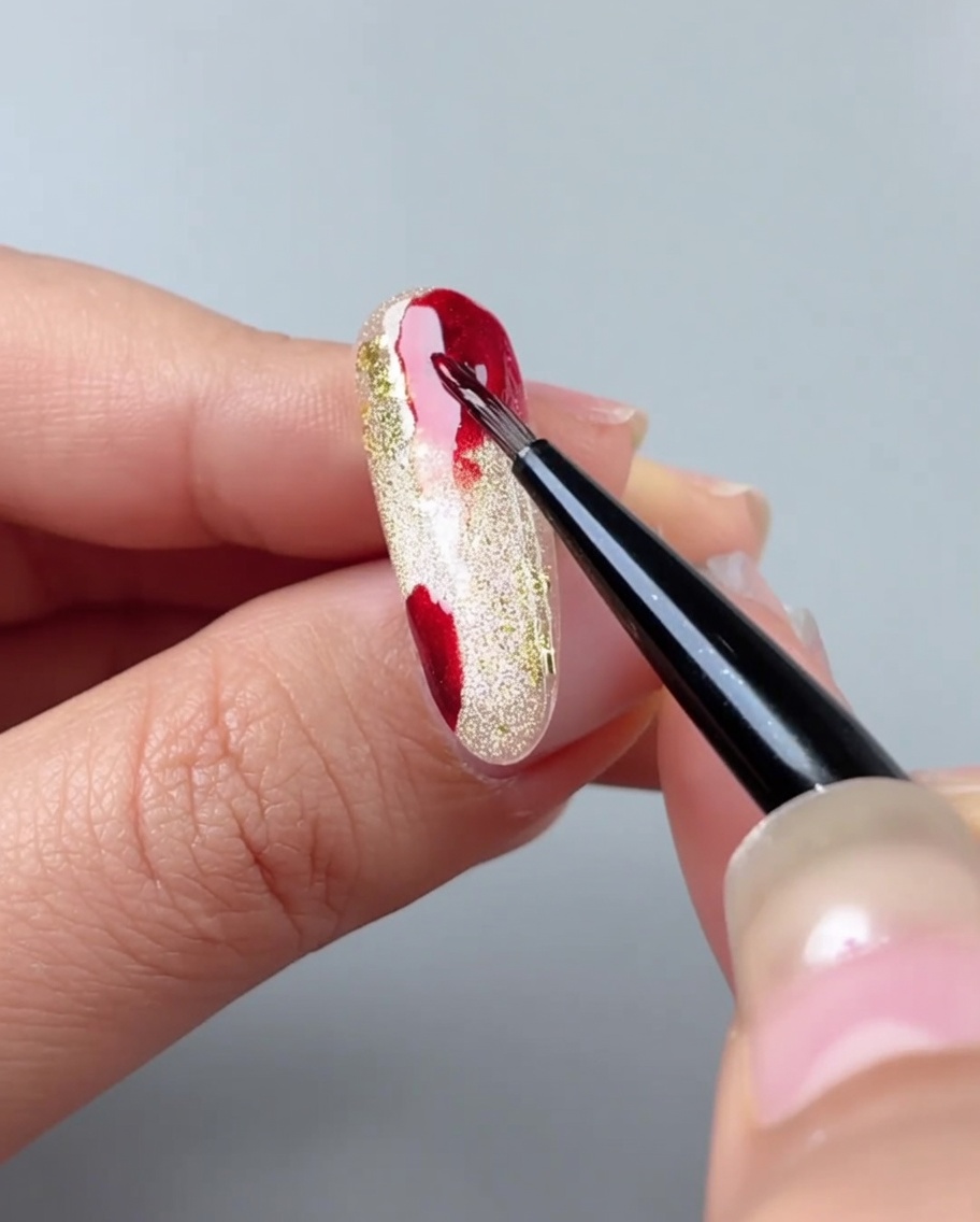 A nail brush blending red gel patches into a gradient using watercolor gel.