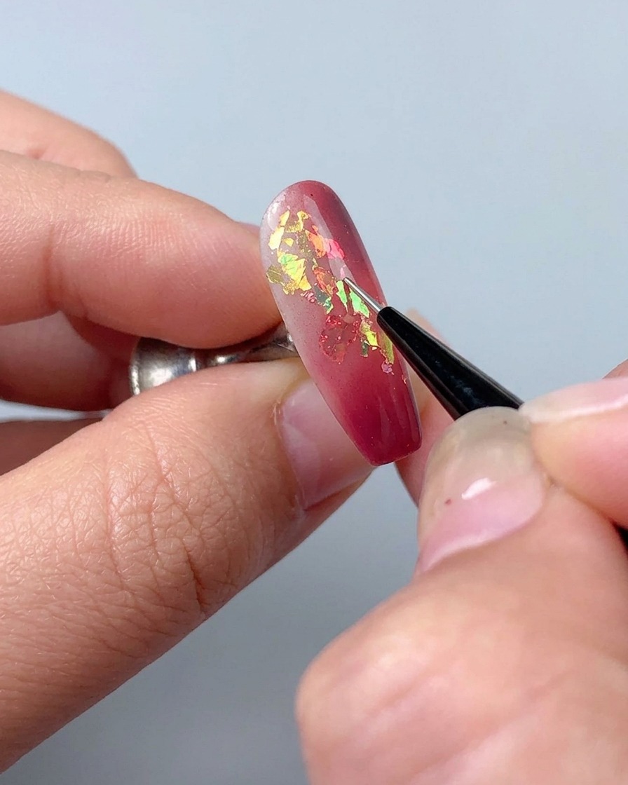 A liner brush being used to draw fine decorative lines with sculpting gel on a manicured nail.