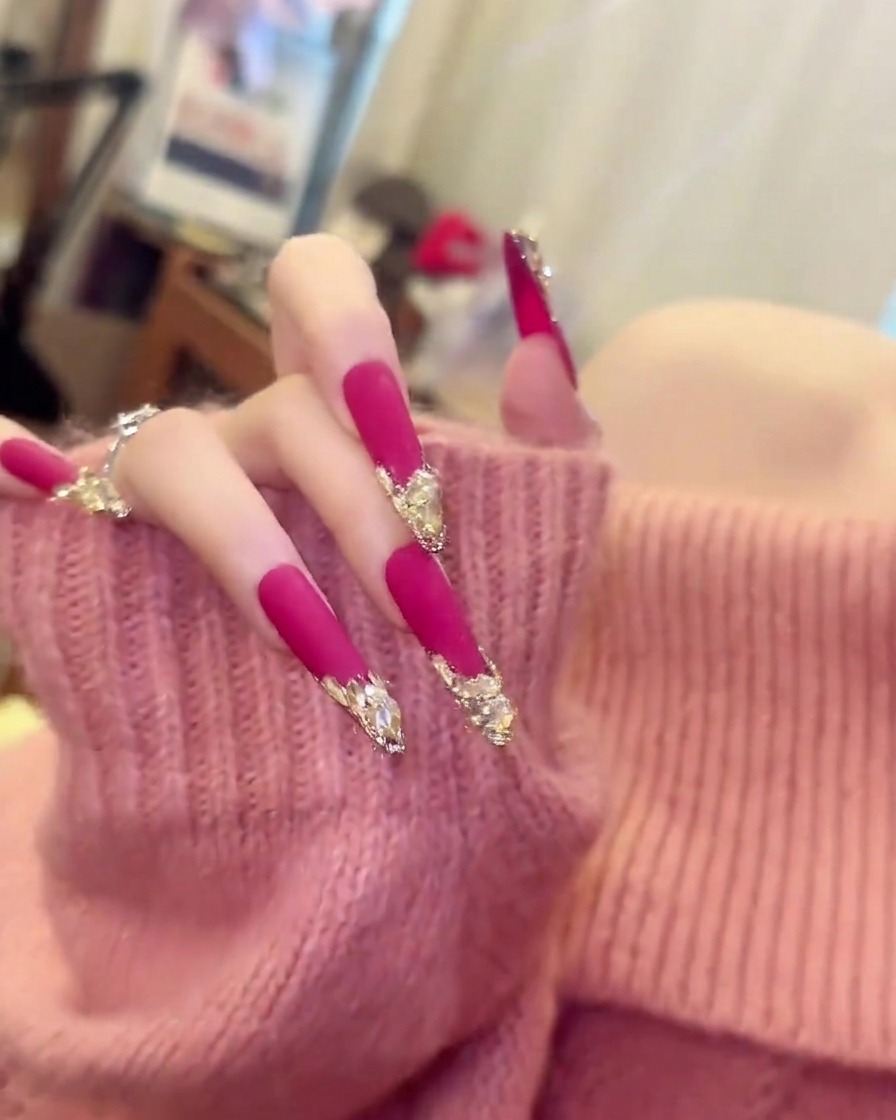 A hand in a soft pink sweater moving slightly to display the length and curvature of long, matte pink almond nails.
