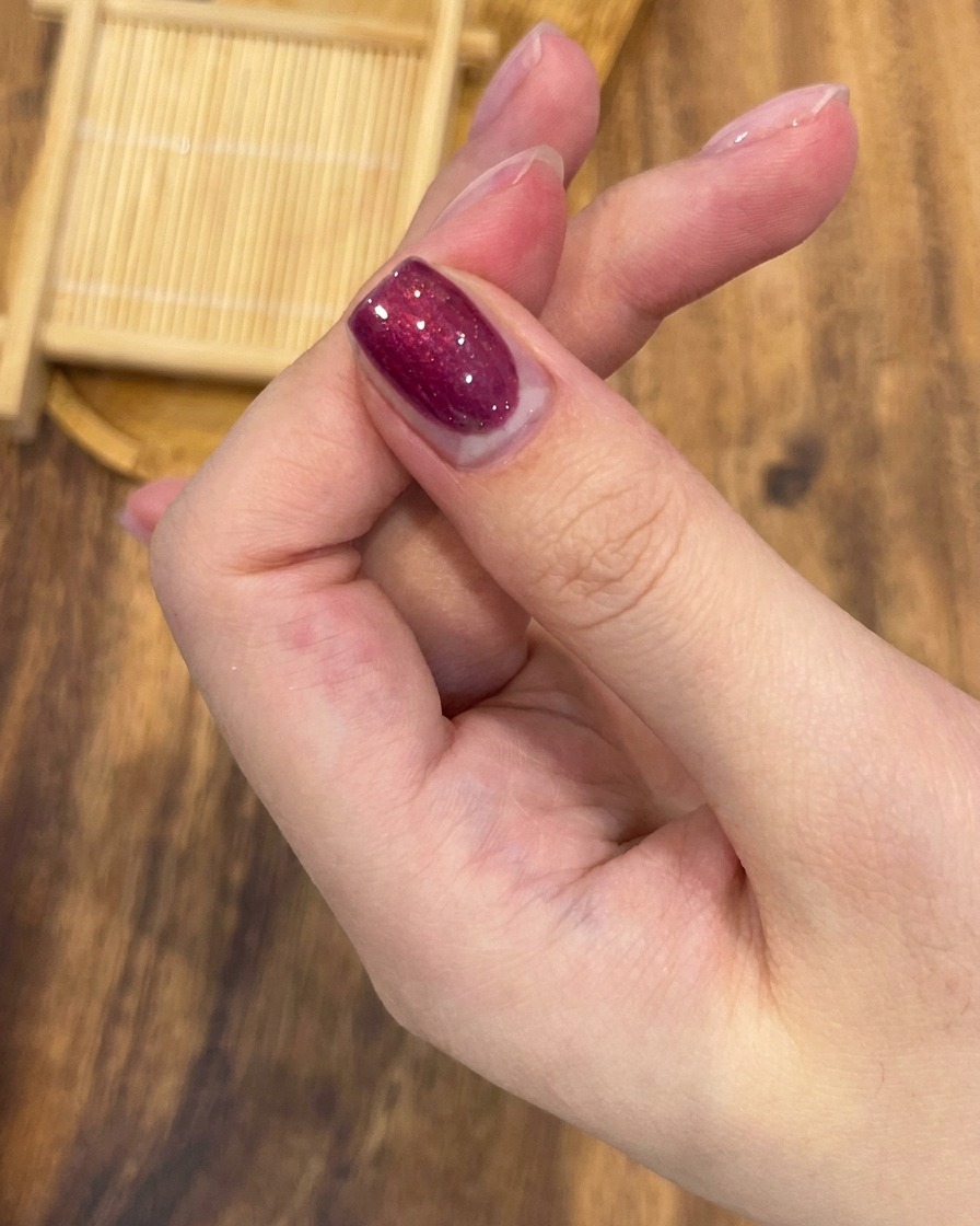 A professional nail brush applying vibrant rose red magnetic gel polish evenly across a fingernail.
