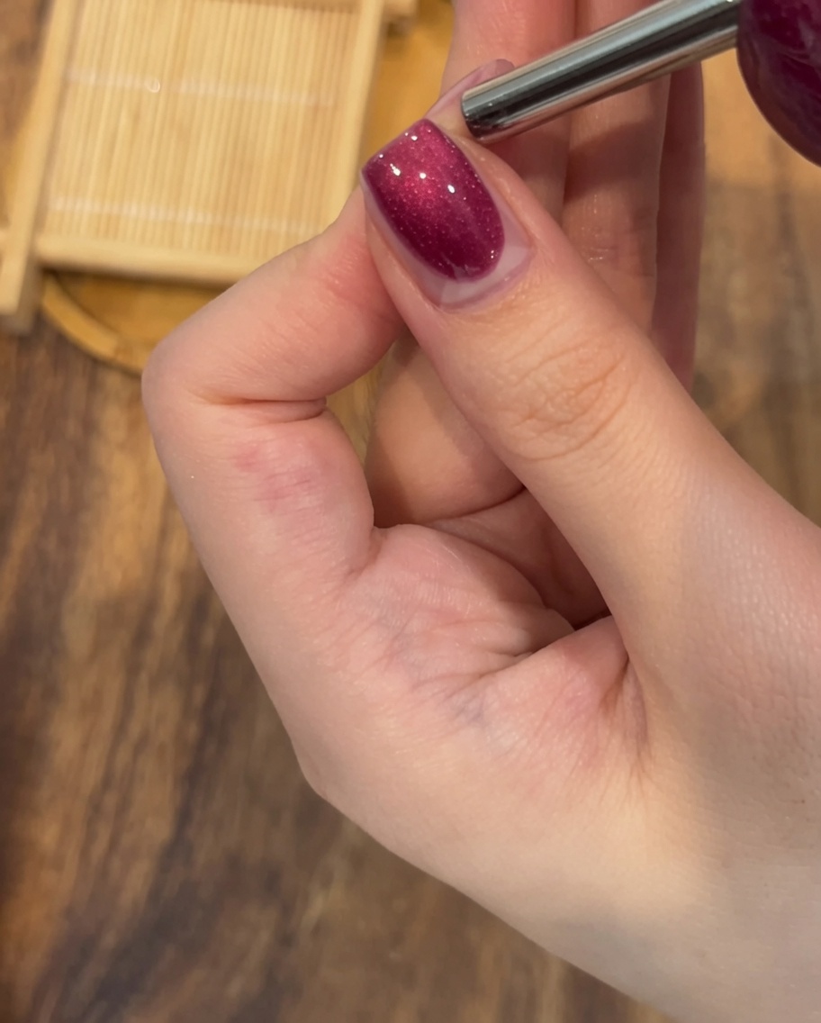 A close-up of a rectangular magnet held steadily over a wet magnetic gel-painted nail to create a prominent shimmer line.