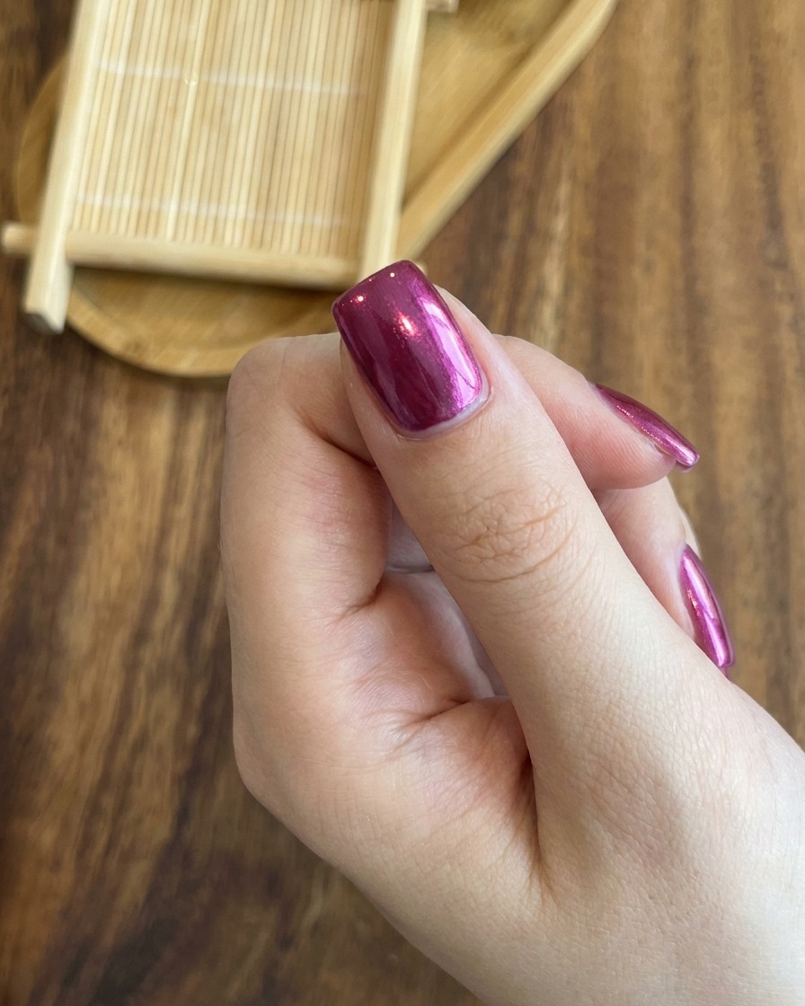A close-up showing a magnet being used to precisely center the bright cat-eye shimmer line on a rose red nail.