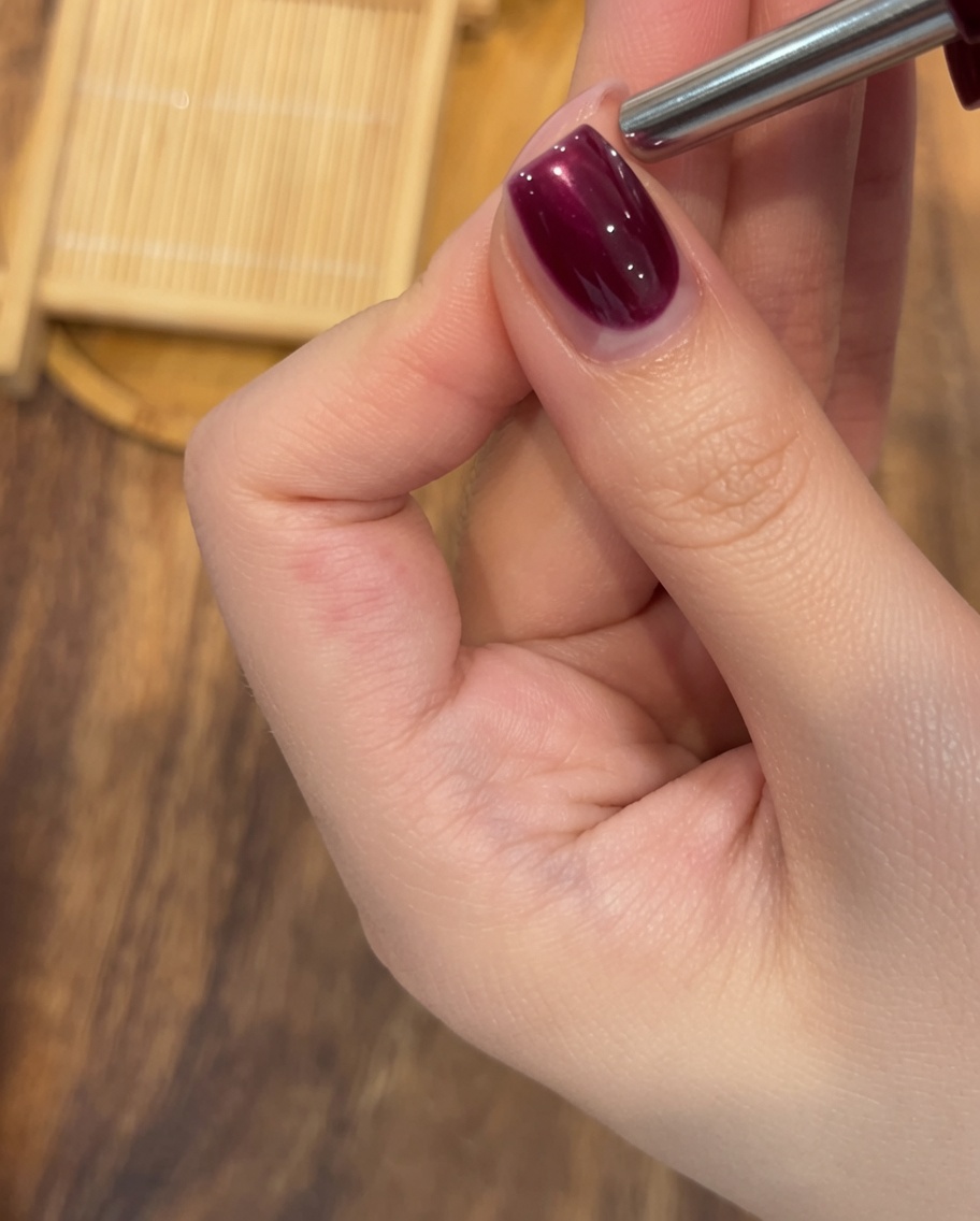 A close-up of a finished rose red magnetic cat-eye nail ready for its final cure under a UV/LED lamp.