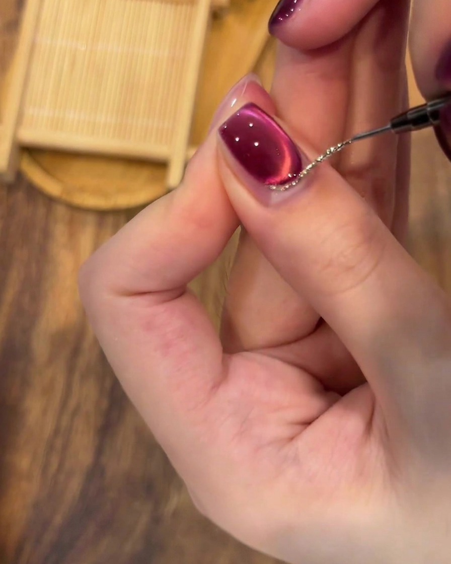 A close-up of a liner brush meticulously refining a silver glitter border at the base of the nail.