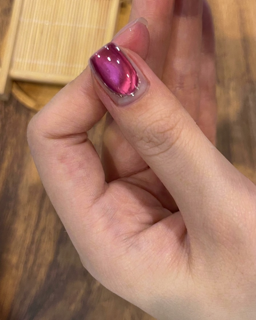 A brush applying a clear, glossy top coat over the finished cat-eye and glitter nail design.