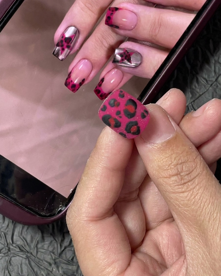 A small nail tip being coated with vibrant hot pink gel polish using a professional nail brush.