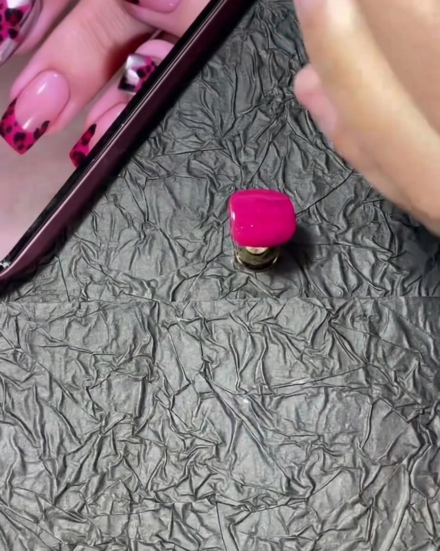 A manicured nail tip being dipped and rotated into a small pot of clear acrylic powder.