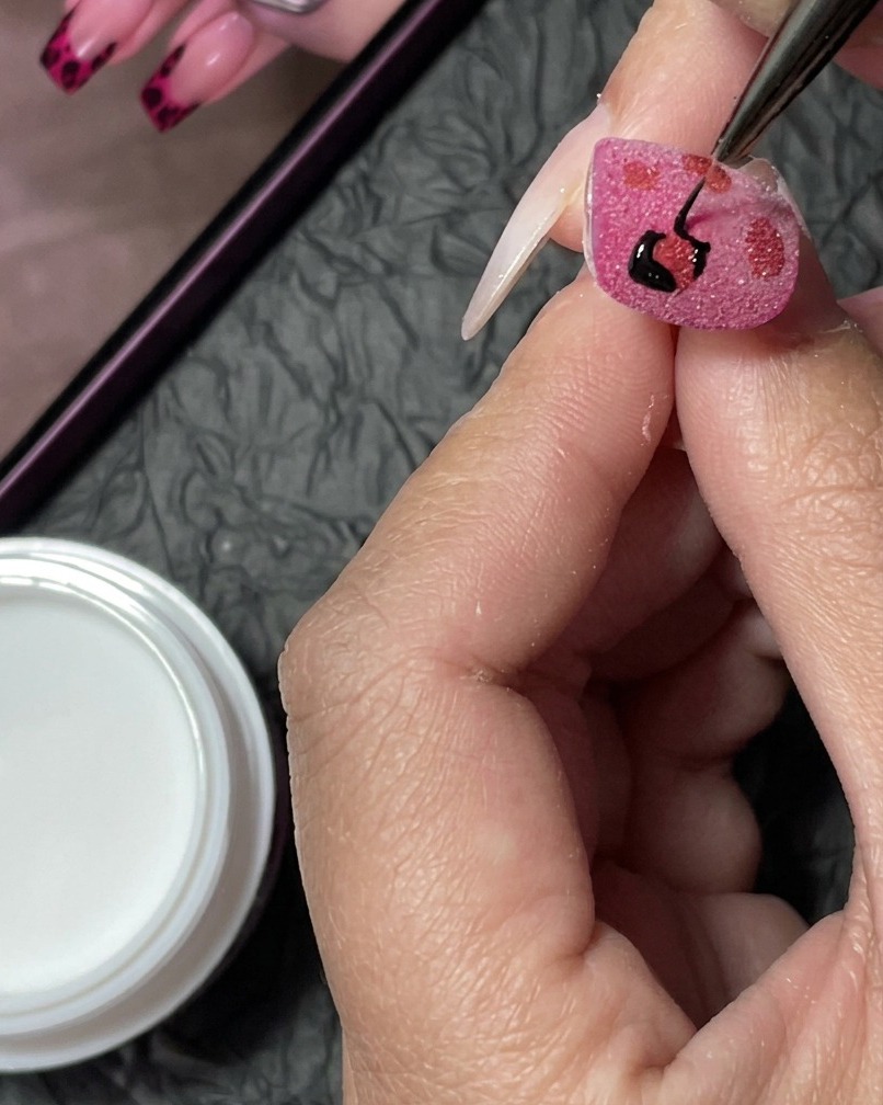 A detailed view showing more black leopard spots being added to fill the gaps on the nail.