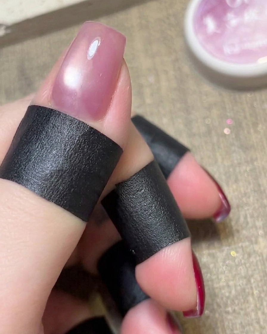 A cylindrical magnet being held over a wet pink cat-eye gel polish on a nail.