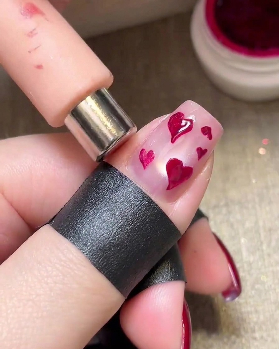 A magnet being held over wet magenta hearts to create a shimmering metallic effect.