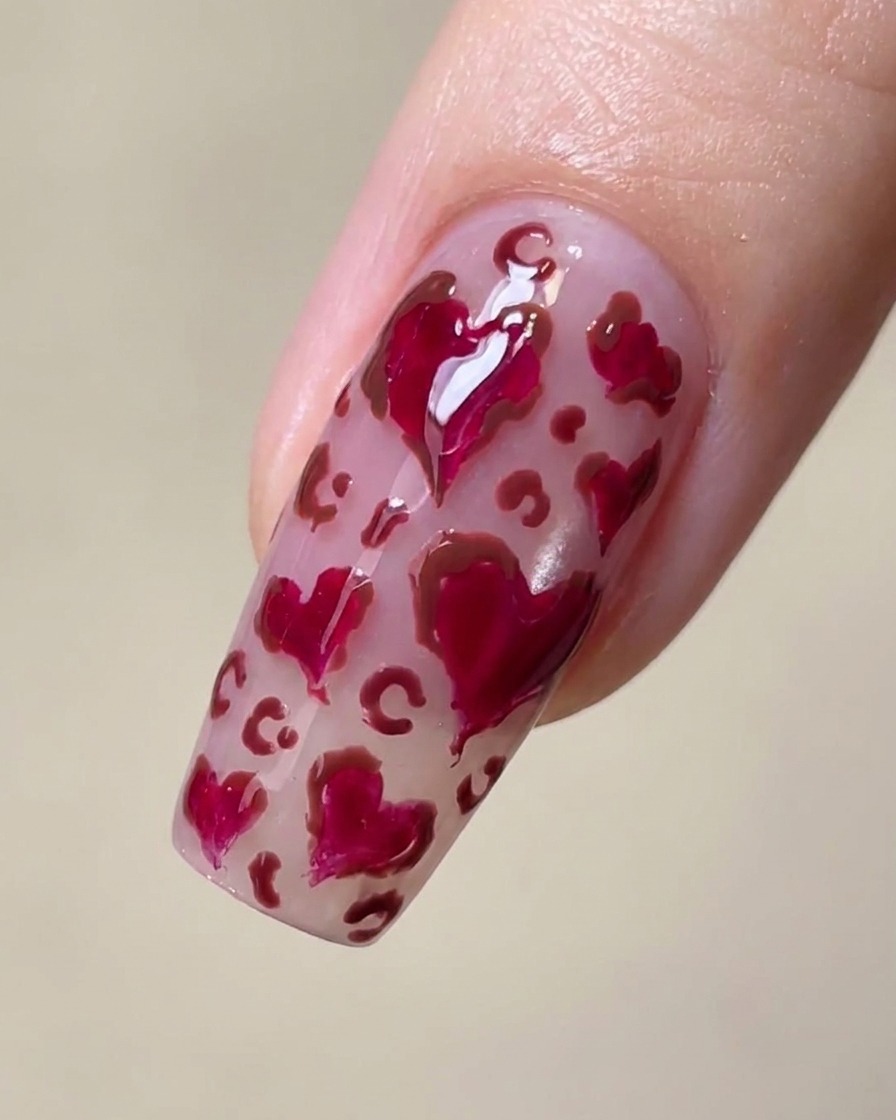 A close-up of a nail with magenta hearts and delicate brown leopard print spots between them.