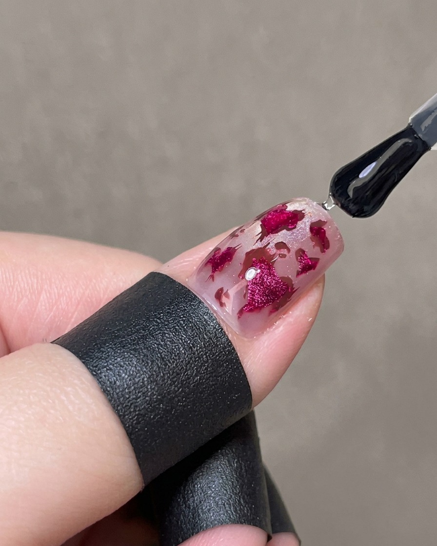 A brush applying a thick layer of clear glossy gel over a decorated nail to encapsulate the pink heart and leopard spot design.