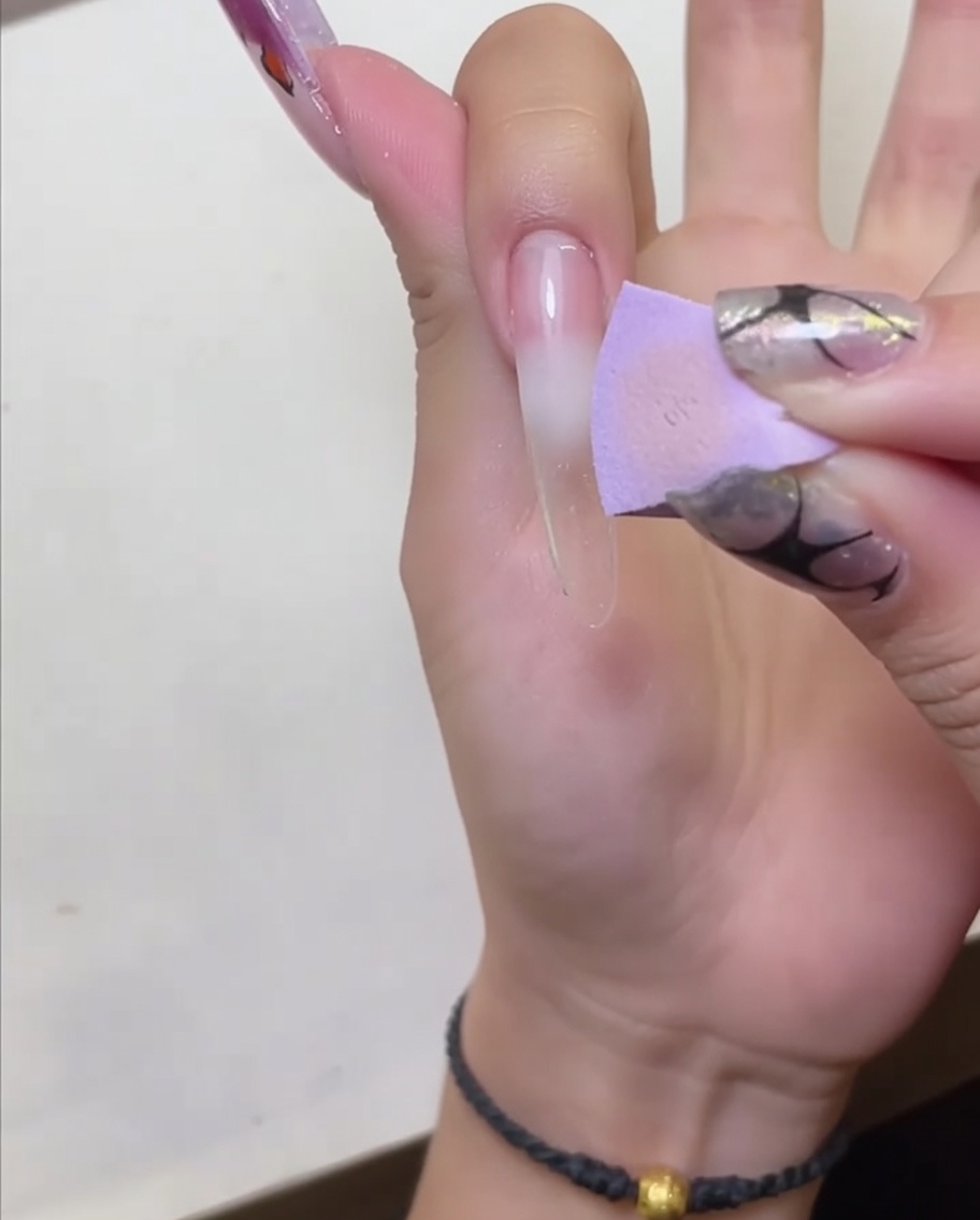 A hand positioned under an LED nail lamp to cure the applied peel-off base coat.