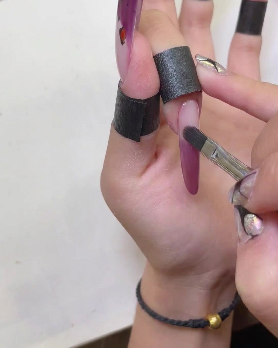 A brush being used to neatly shape and smooth the edges of the red cat-eye gel french tip.