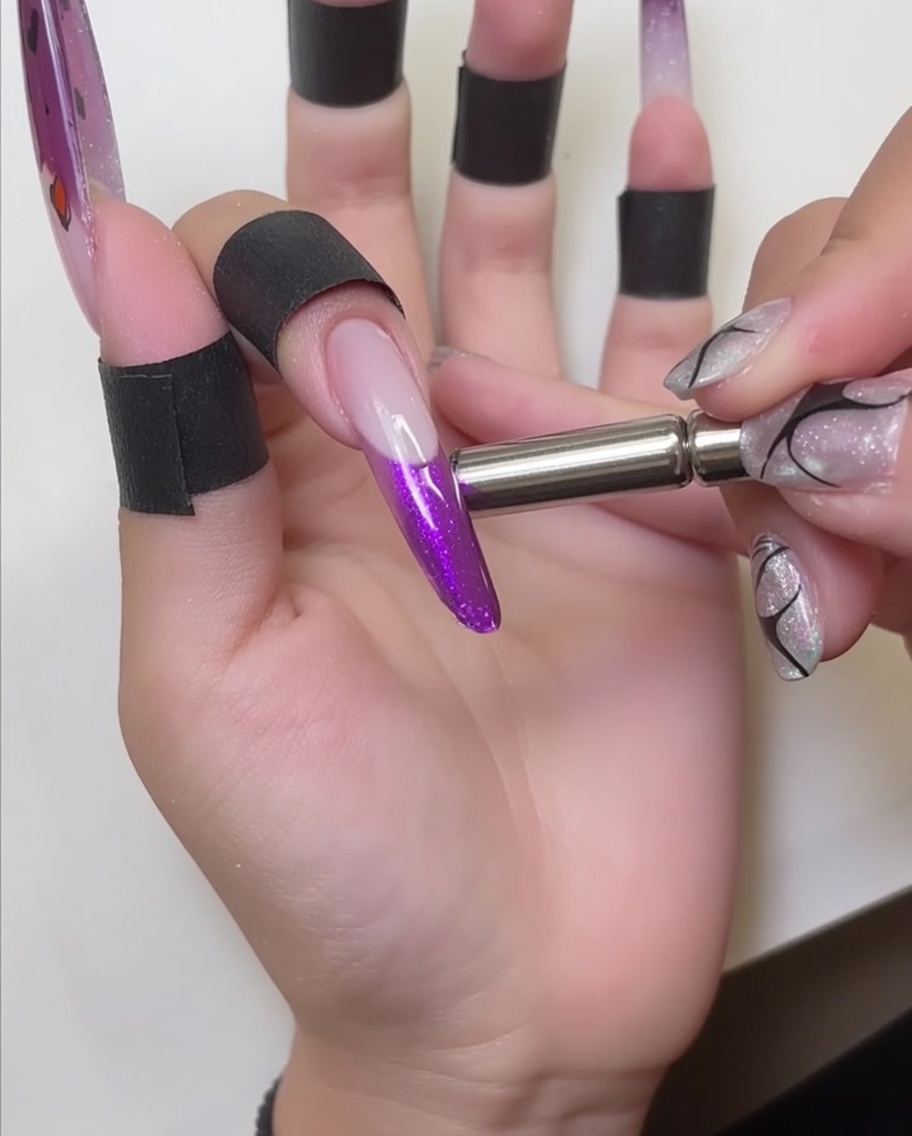 A metal magnetic wand held close to a nail tip, showing the shimmering effect being drawn into the red cat-eye gel.