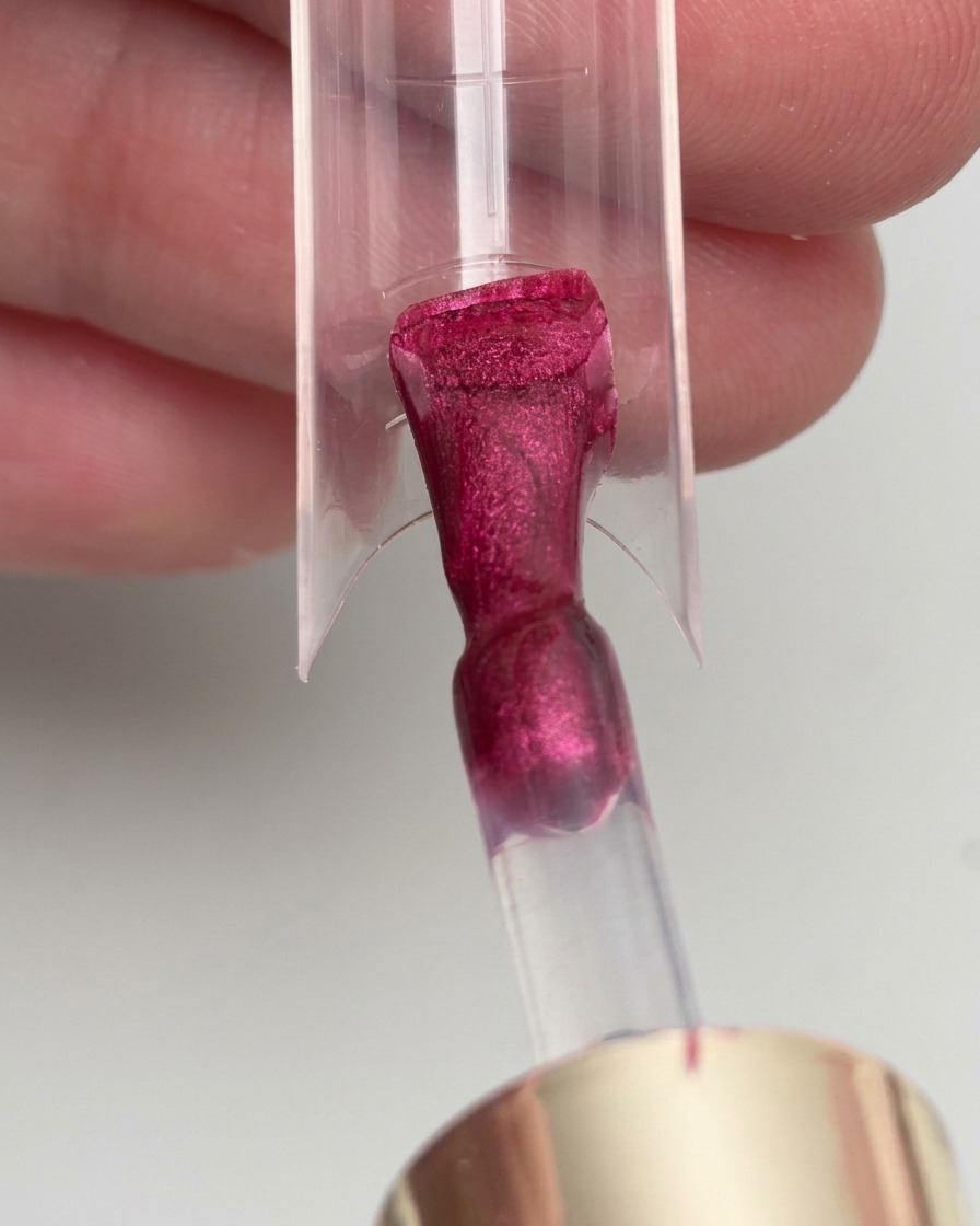 A brush applying magenta gel polish onto a clear nail extension form.