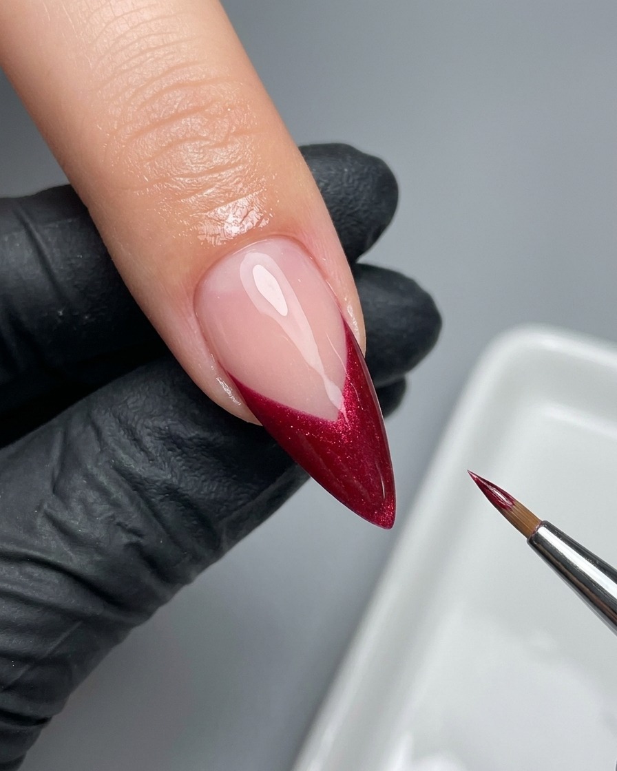 A fine liner brush carefully perfecting the edge of a magenta French tip on a nail.