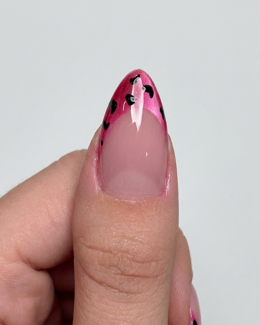 A liner brush adding delicate black outlines around dots on a magenta French tip.
