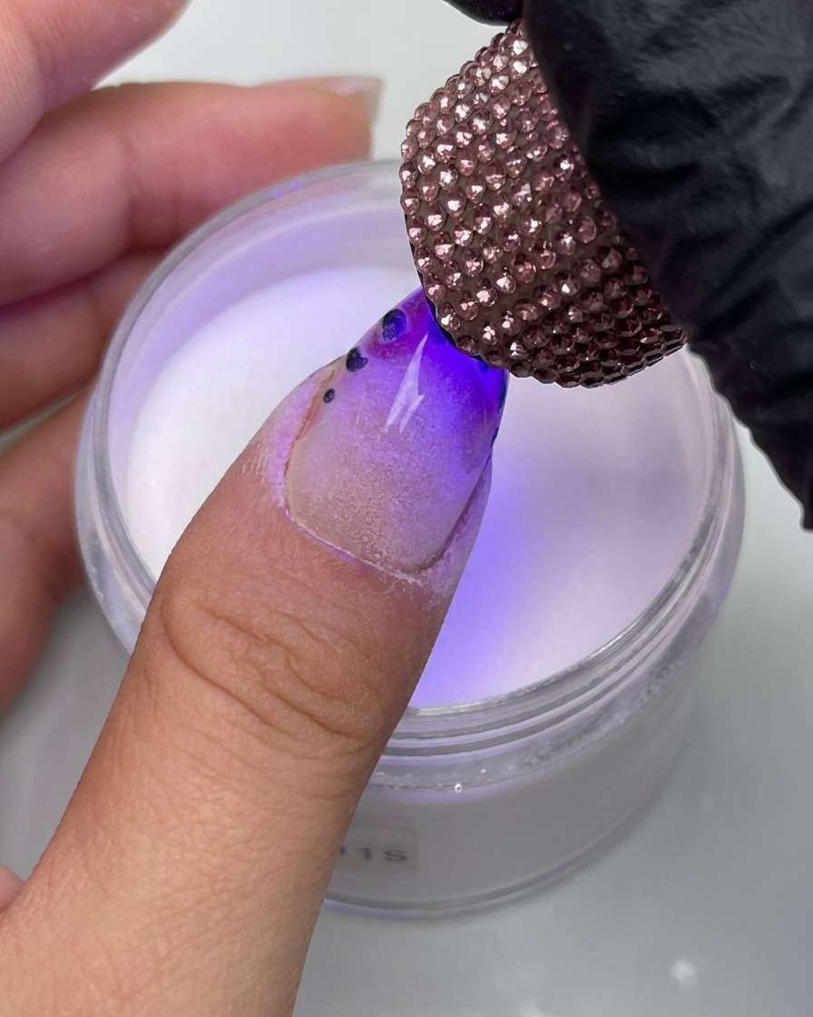 A close-up view of a finger with a leopard print design being placed under a decorative rhinestone-covered UV lamp.