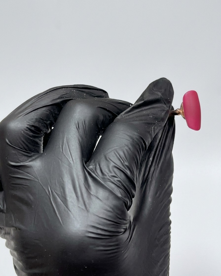 A close-up of a nail tip fully coated in a vibrant rose red gel polish, with a smooth, glossy, uncured finish.