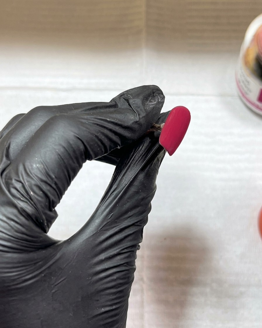 A close-up of a fluffy brush sweeping excess powder off a matte, textured red nail surface.