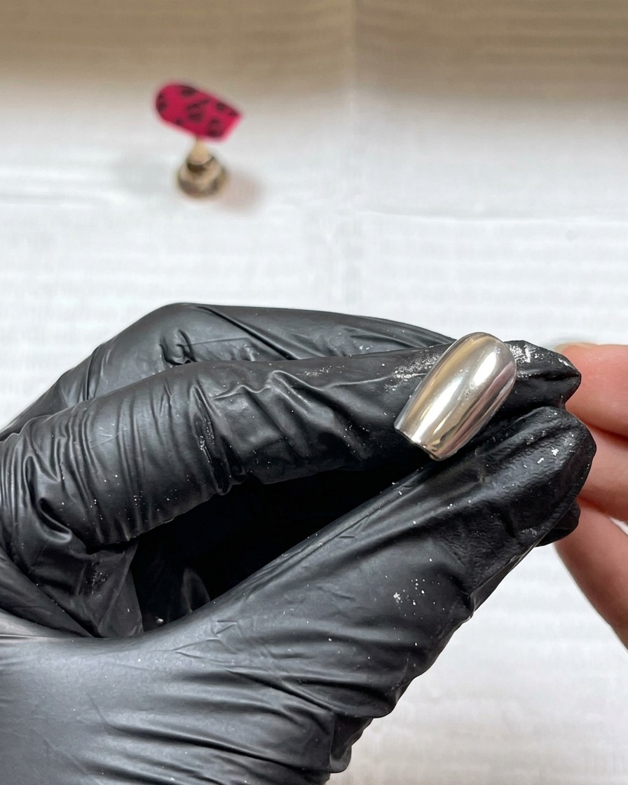 Clear acrylic powder being sprinkled over the wet black gel details on the nail.